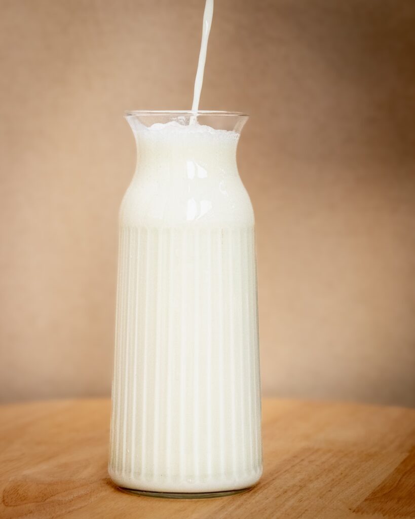 Organic cream-top milk being poured into a glass pitcher, showing natural creamy texture
